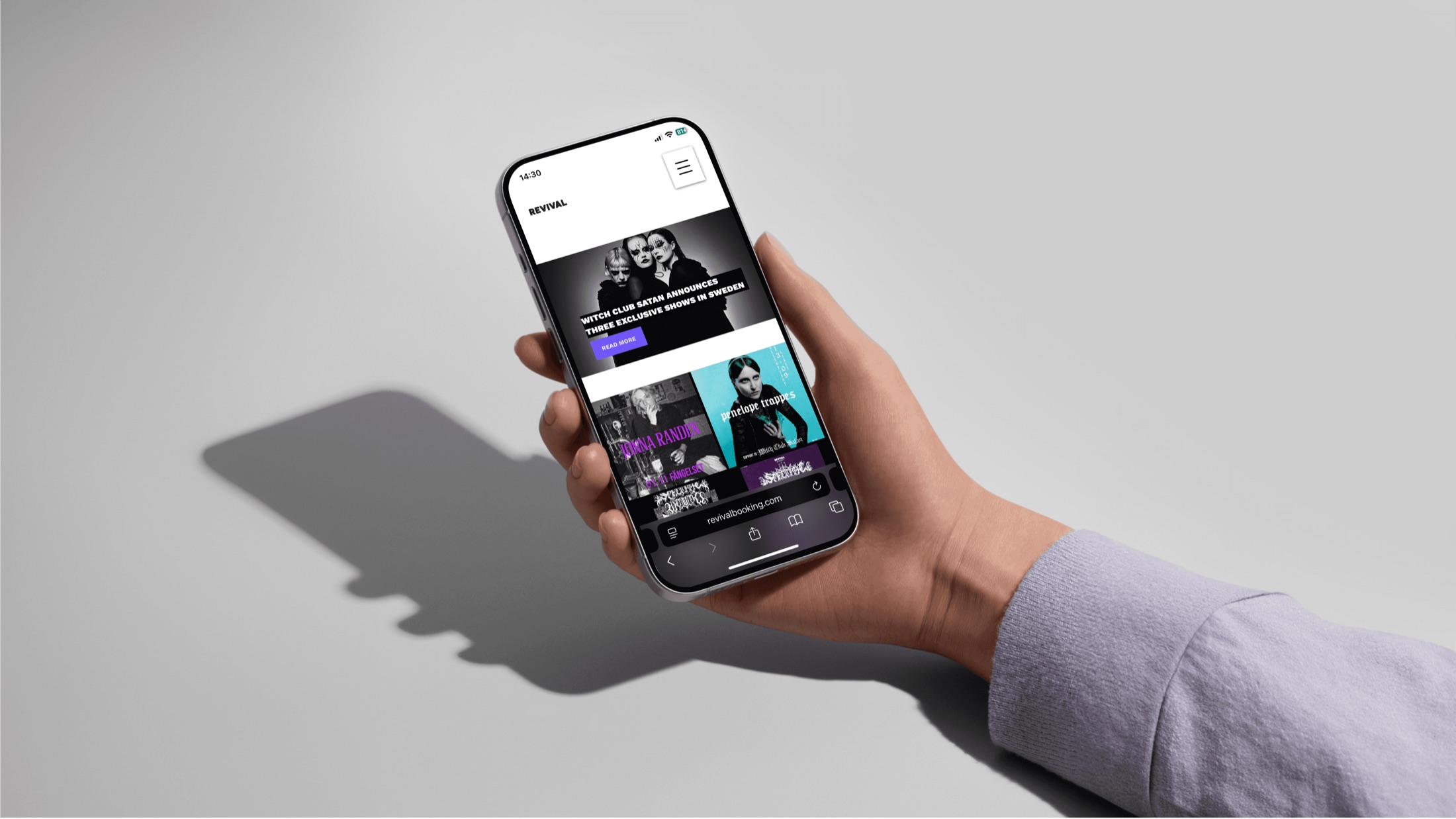 A hand holding a phone showing Revival Booking's mobile home page with the Witch Club Satan announcement and upcoming show posters.